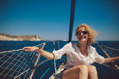 Cheerful mid adult woman sitting on sailboat in sea during summer