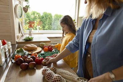 Mother and daughter unpacking fresh groceries in kitchen