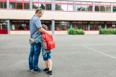 Happy dad hugs the child of the schoolboy and escorts him to school at the beginning of the lessons.