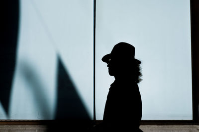 Silhouette man wearing hat standing against wall