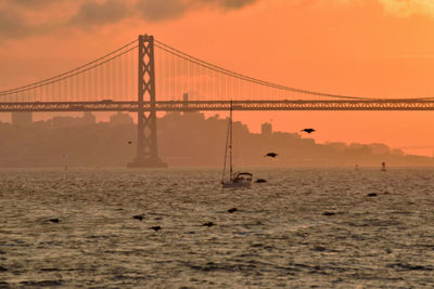 Suspension bridge over sea against sky during sunset