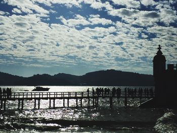 Silhouette of bridge over sea against cloudy sky