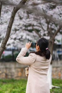 Rear view of man photographing against trees