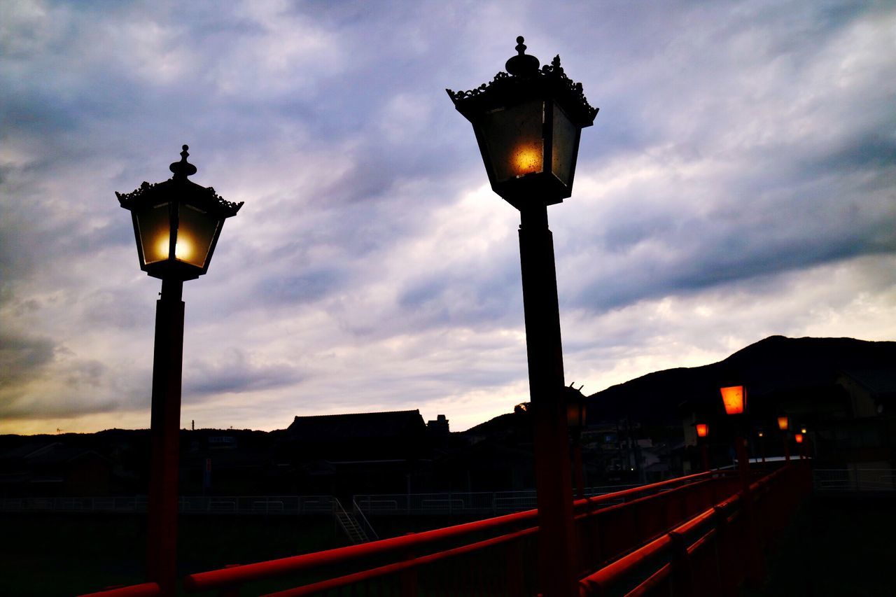 street light, illuminated, dusk, lighting equipment, built structure, architecture, building exterior, lamp post, railing, lit, in a row, cloud, sky, dark, outdoors, city life, cloud - sky, electric light, no people, outline