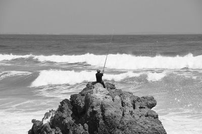 Man fishing in sea against clear sky