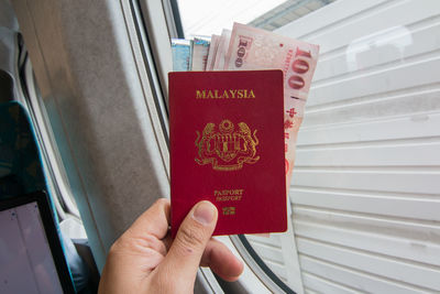 Cropped hand holding malaysian passport with paper currency in train