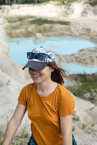 Happy young smiling woman traveler in cap running on sand of clay quarry with blue turquoise water