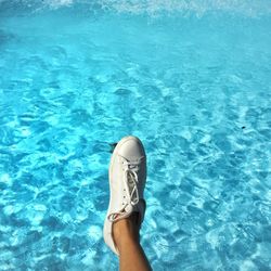 Low section of person wearing white shoe against swimming pool