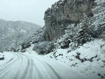 Snow covered road by mountain against sky