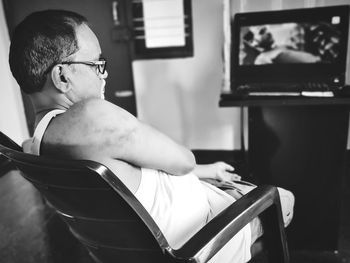 Side view of man watching tv while sitting at home