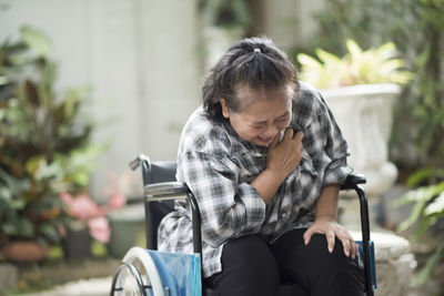 Disabled woman suffering from chest pain while sitting on wheelchair in park