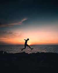 Silhouette man jumping over sea against sky during sunset