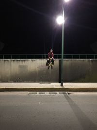 Full length of man sitting by street light at night