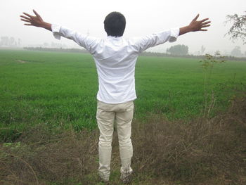 Rear view of man with arms outstretched standing on field