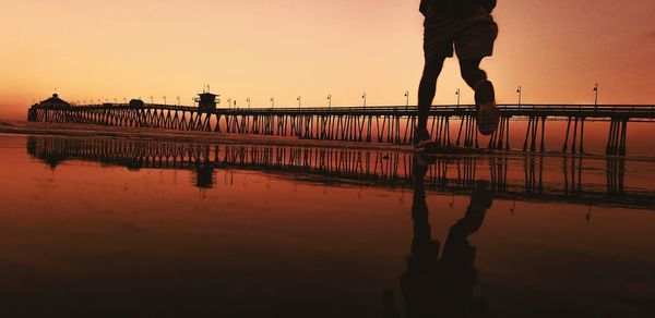 Low section of man walking on shore against sky during sunset