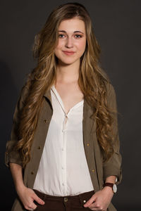 Portrait of young woman with blond hair standing against black background