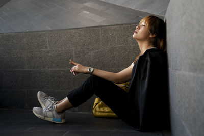 Side view of businesswoman with eyes closed sitting by wall