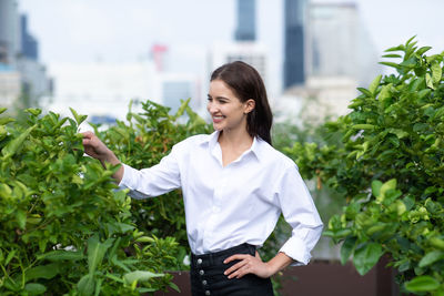 Young woman smiling while standing against plants