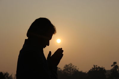 Side view of man praying against sky during sunset