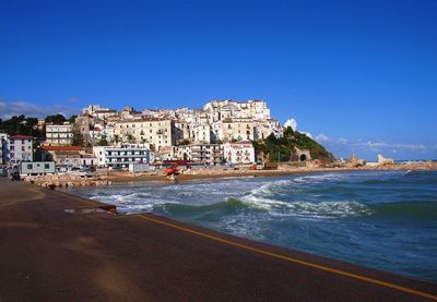 Buildings by sea against blue sky