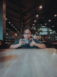 Young teen wearing glasses sitting at the table is using a mobile phone.