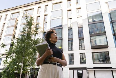 Businesswoman with laptop in front of office building