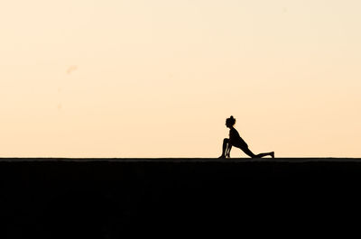 Silhouette woman exercising against clear sky during sunset