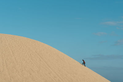 Man climbing on sand in desert against sky