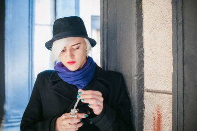 Close-up of young woman preparing electronic cigarette by column