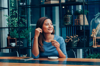 Young woman looking away while sitting on table at restaurant