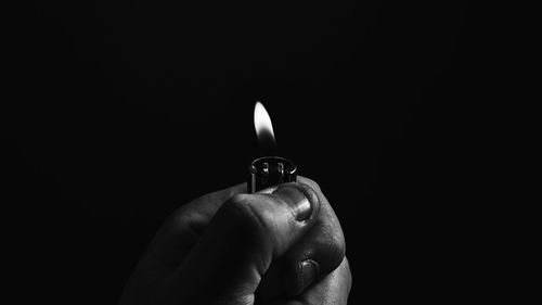 Close-up of hand holding candle against black background