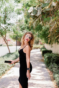 Portrait of a beautiful girl in sunglasses and an elegant black dress with a phone in her hand