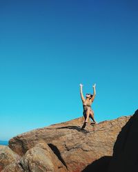 Woman sitting on rocky shore against clear blue sky