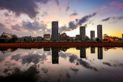 Reflection of buildings in lake against sky during sunset