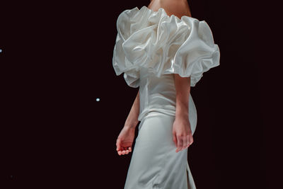 Fashion details of white silky bridal dress. fashion model walking on black background