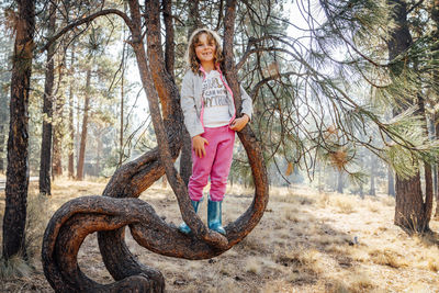 Smiling girl in sweats and rubber books standing on tree branch