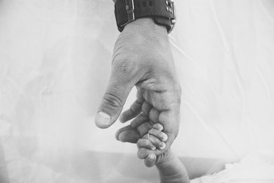 Cropped image of father holding son hand at home