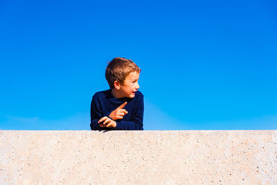 Boy looking away against blue sky