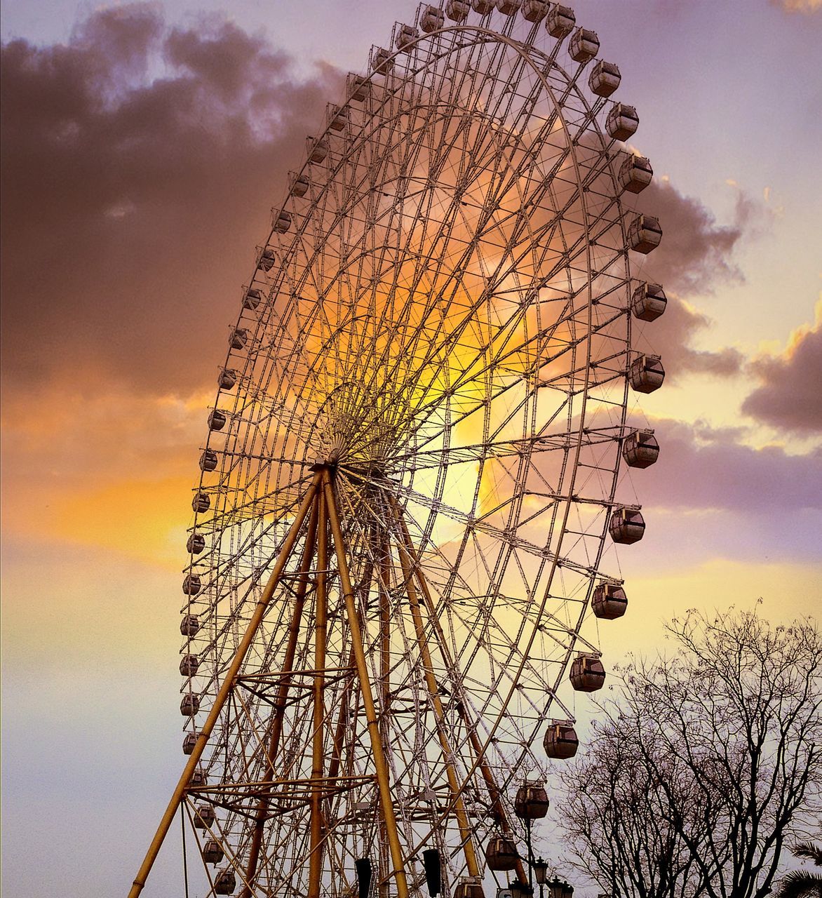 low angle view, sky, amusement park, ferris wheel, amusement park ride, arts culture and entertainment, cloud - sky, tall - high, sunset, cloudy, built structure, outdoors, cloud, silhouette, dusk, no people, tree, nature, architecture, tower