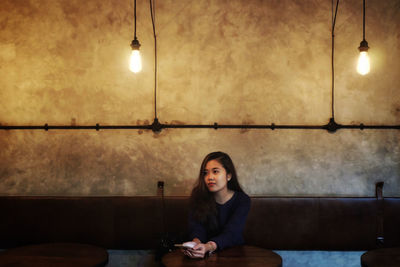 Portrait of young woman sitting on table against illuminated wall