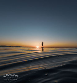 Silhouette person on sea against clear sky during sunset