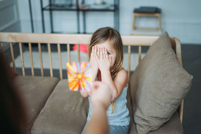 Cropped hand of girl holding decoration by friend with hands covering face