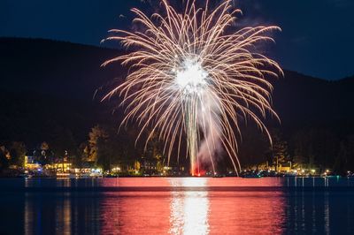 Illuminated fireworks by lake against sky at night