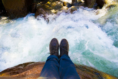 Low section of man sitting on rock over river