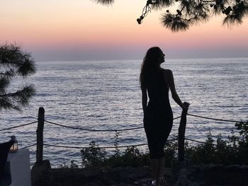 Silhouette woman standing on beach against sky during sunset
