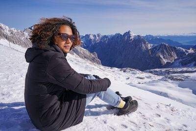 Pretty young woman is sitting in the snow, looking at the mountain view/ skiing area/ zugspitze