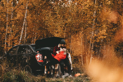 A romantic couple in love in warm sweaters is walking traveling by car in the autumn forest in fall