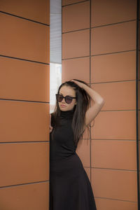 Young woman wearing sunglasses while standing by wall