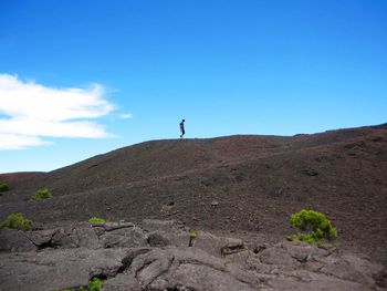 Low angle view of man walking on mountain against blue sky