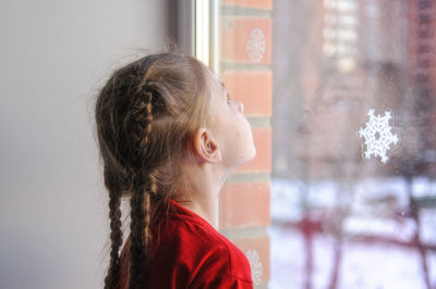 Side view of girl looking through window during winter